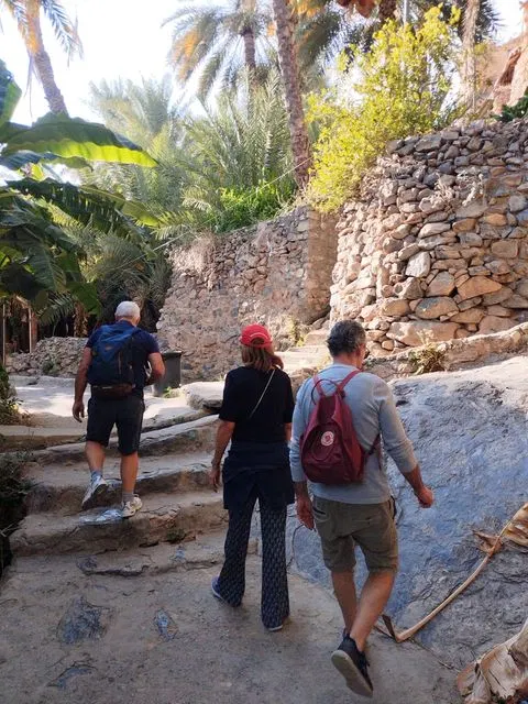 Palmiers et habitat traditionnel dans un paysage aride, avec des personnes visibles.