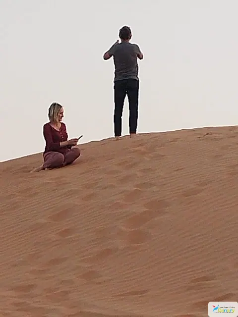 Relief de dunes dans un vaste paysage désertique, avec des personnes visibles.